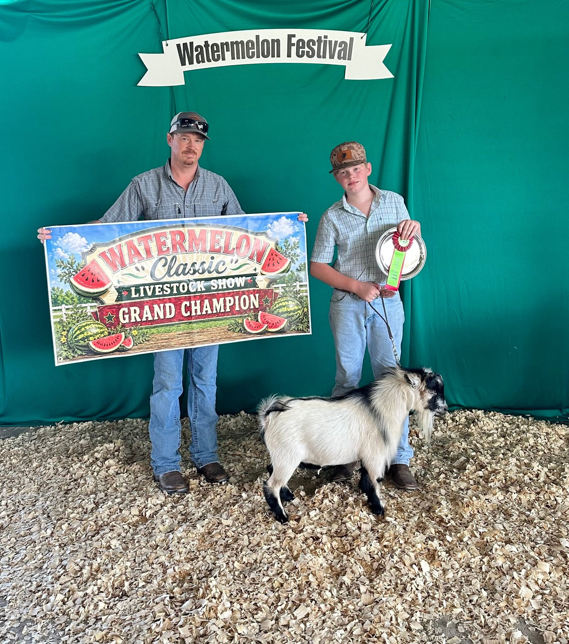 A man and a boy standing by a white and black goat. Watermelon Festival. Watermelon Classic Livestock Show Grand Champion.